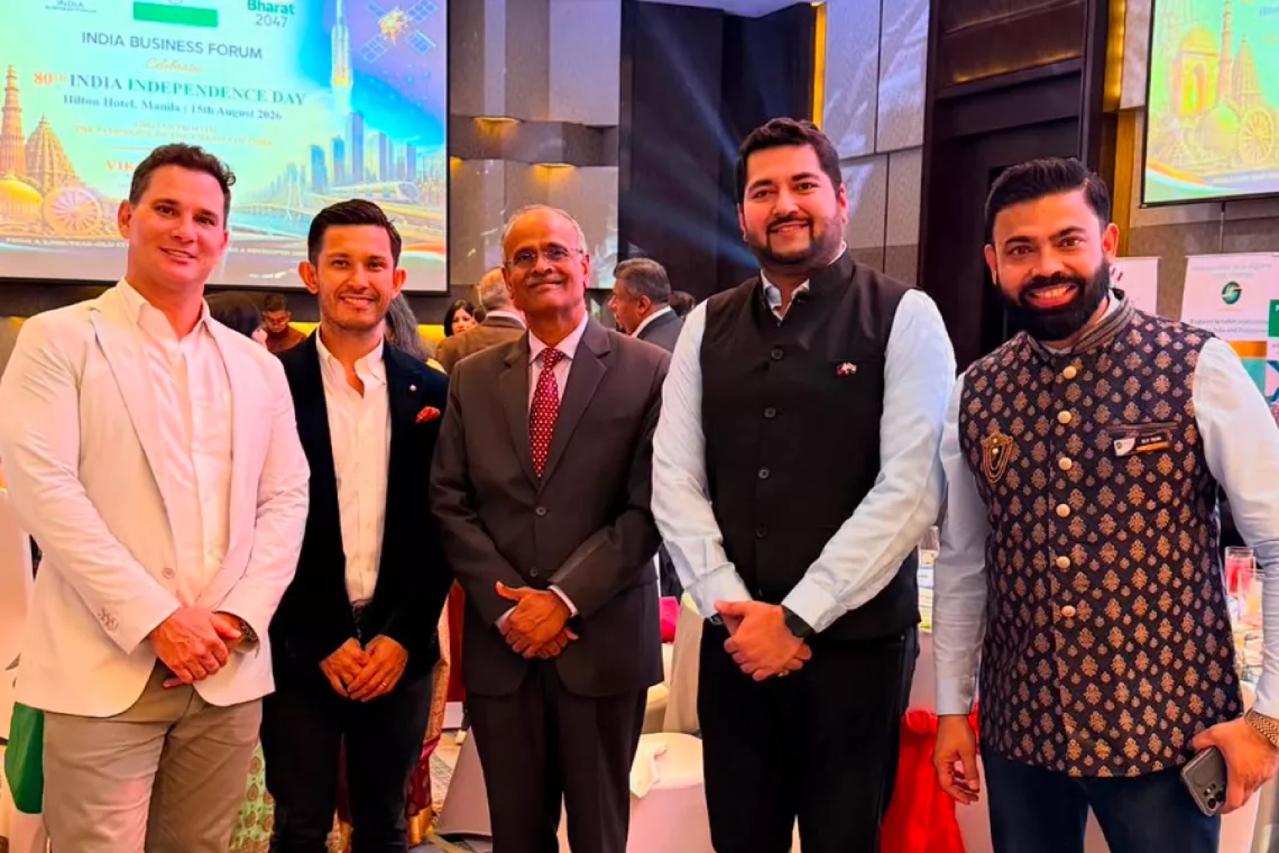 Five guests standing together at a reception in front of screens showing an India Business Forum panel