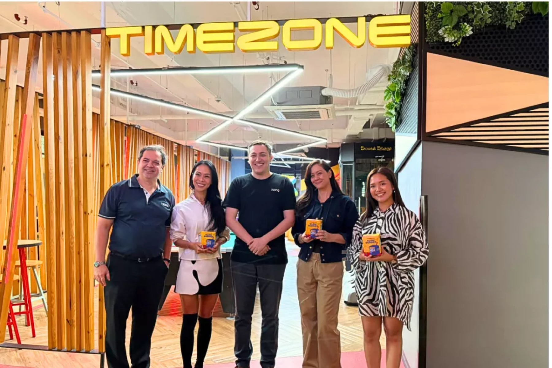 Five people standing under an illuminated Timezone sign in a wood-panelled venue