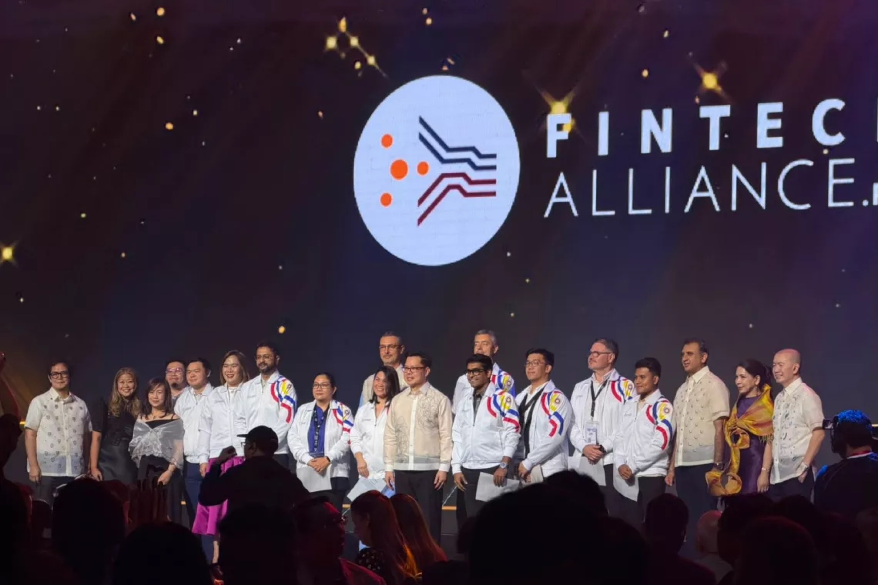 A line of guests on a darkened stage beneath a projected Fintech Alliance mark