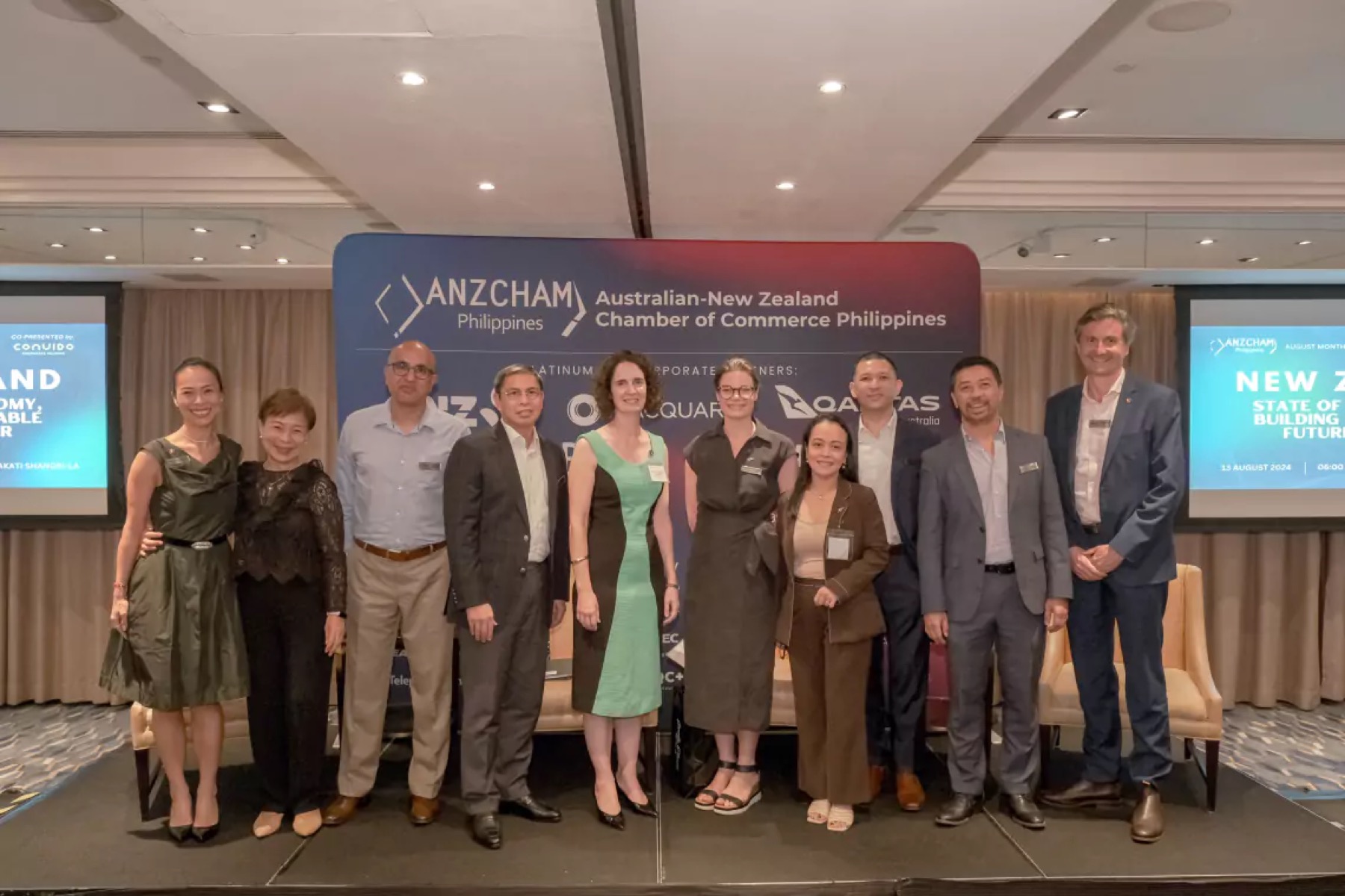 About ten guests standing in a line in front of an ANZCHAM Philippines banner in a function room