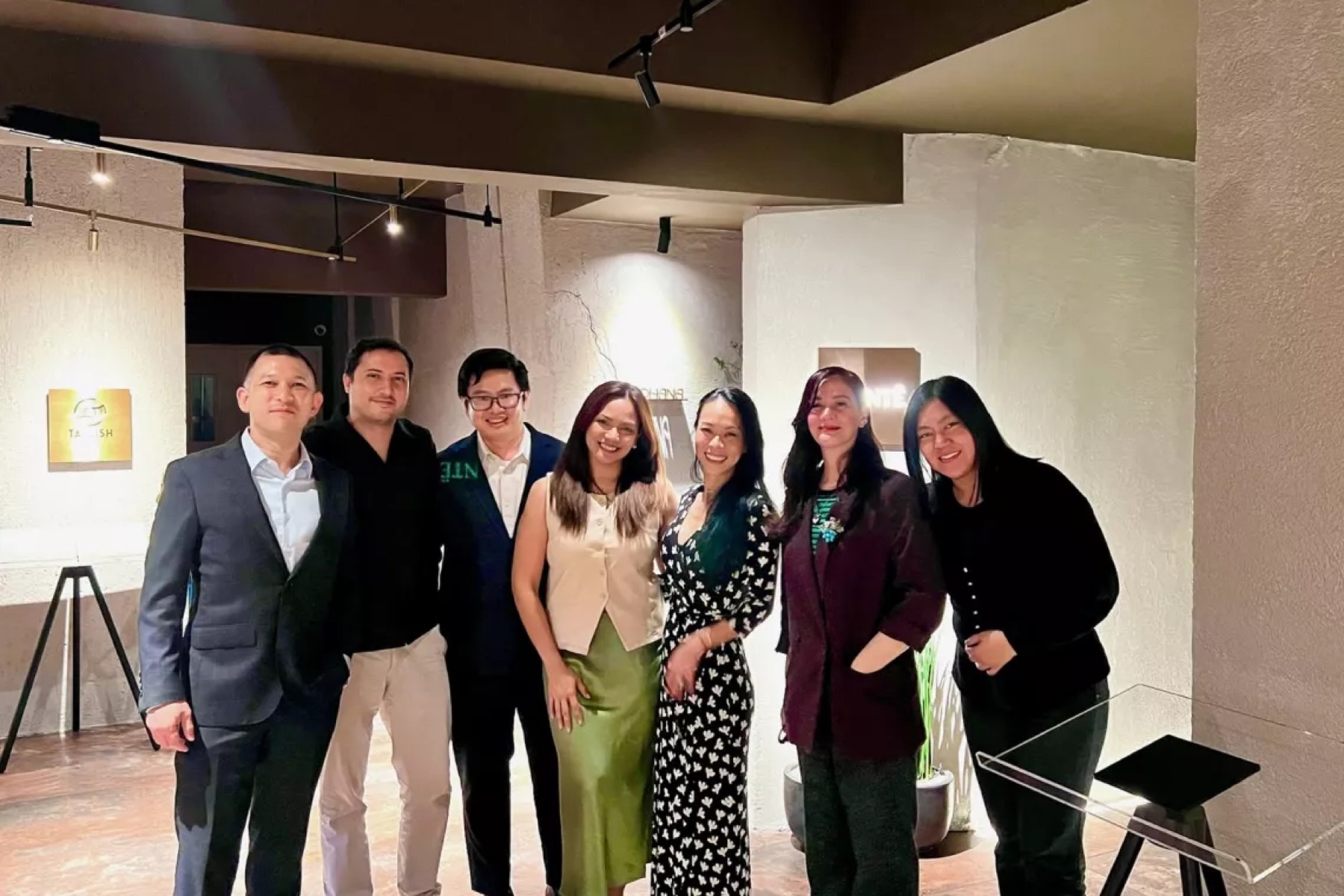 Seven guests standing together in a gallery space hung with framed pictures
