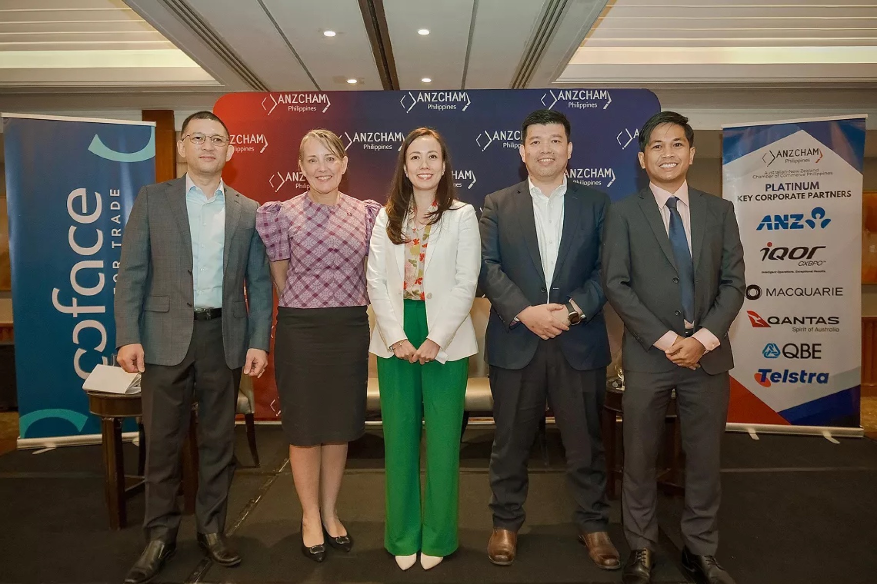 Five guests standing in front of an ANZCHAM Philippines banner beside a partner display board